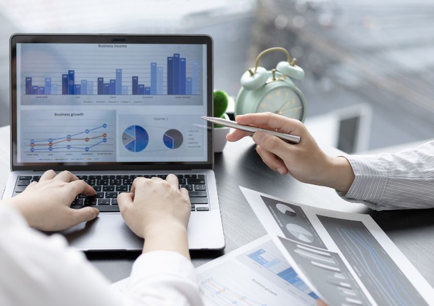Two property managers in dress shirts examine business figures and marketing data on a silver laptop.