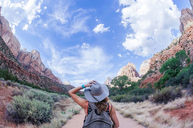 person with backpack and hat in a path surrounded by canyons in the desert.